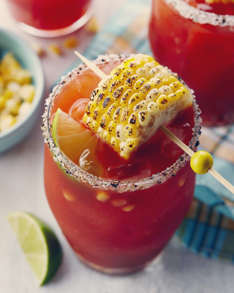 Caesar with lime and corn kernels inside plus a small corn on the cob resting on the glass for garnish