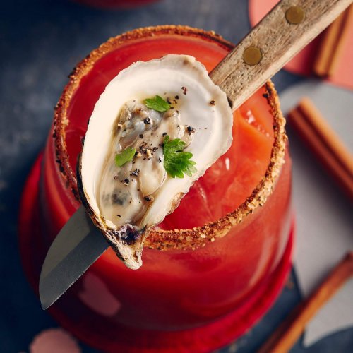 top down view of oyster on knife resting on full Caesar glass